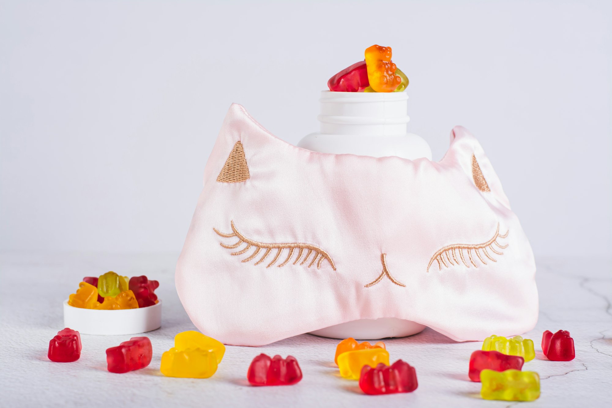 Gummy sleep vitamin supplements and sleep mask next to bottle on table