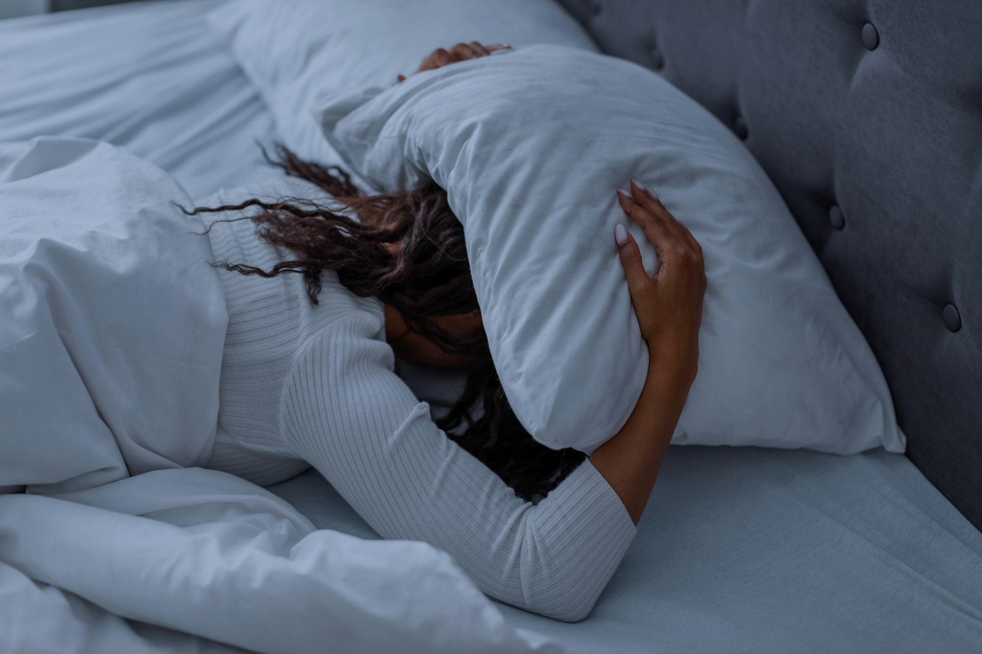 Stressed black woman covering head under pillow lying in bed